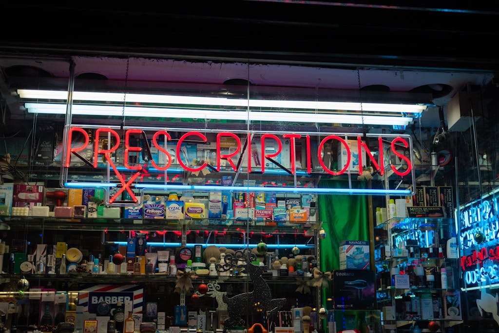 Illuminated neon pharmacy sign with prescriptions on a storefront at night.